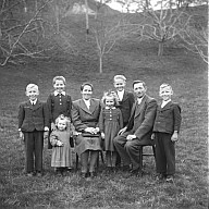 Ganzfigurportrait einer neunköpfigen Familien, davon zwei Kinder im Vorschul- und die fünf anderen im Schulalter. 
