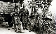 Vier Soldaten der Wehrmacht vor einigen Tafeln, die auf Partisanen weisen 