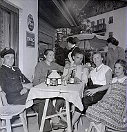 Ein Dorffest: Zwei Frauen, zwei Männer und ein Kind sitzen an einem Tisch vor einer Gaststätte 