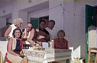 Personengruppe in sommerlicher Kleidung auf der Terrasse eines Hauses. 
